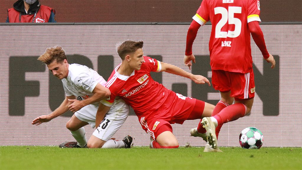 Ein Fußballspieler fällt im Zweikampf zu Boden, während ein anderer Spieler kurz davor ist, ihn zu erreichen.