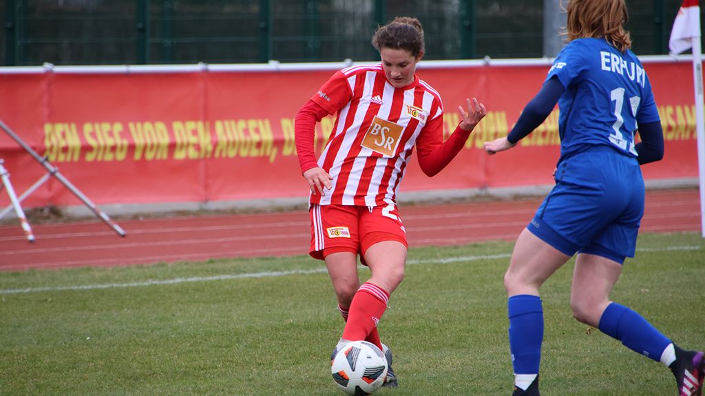 Two female soccer players on the field, one in red and white stripes, the other in a blue uniform, fighting for the ball.