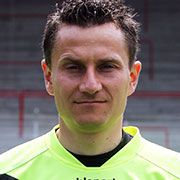 Ein Portrait eines Mannes in einem leuchtend gelben Sporttrikot, mit kurzem, dunklem Haar und ernstem Ausdruck.