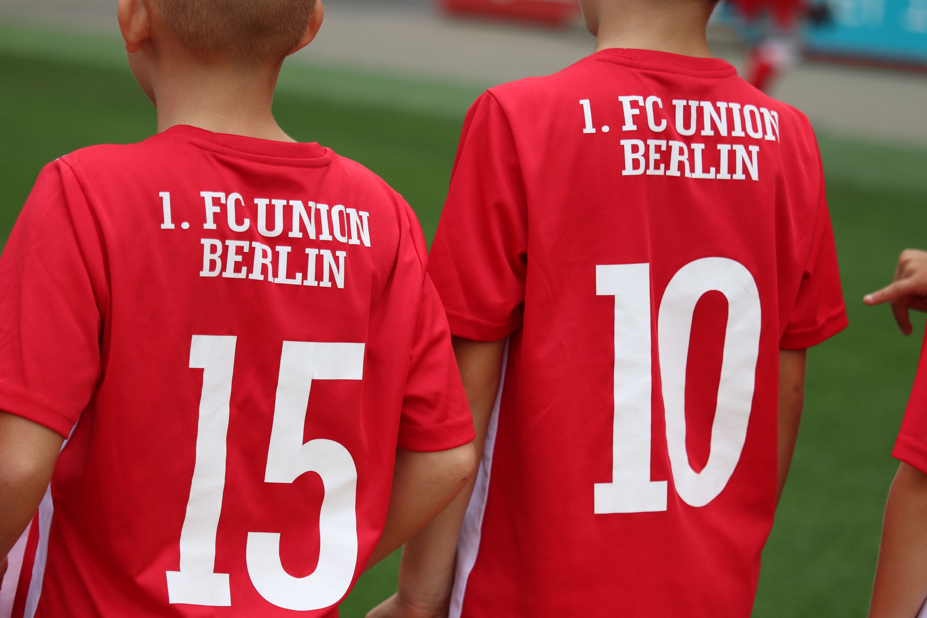 Zwei Kinder in roten Fußballtrikots mit den Zahlen 15 und 10 sowie dem Schriftzug "1. FC UNION BERLIN".