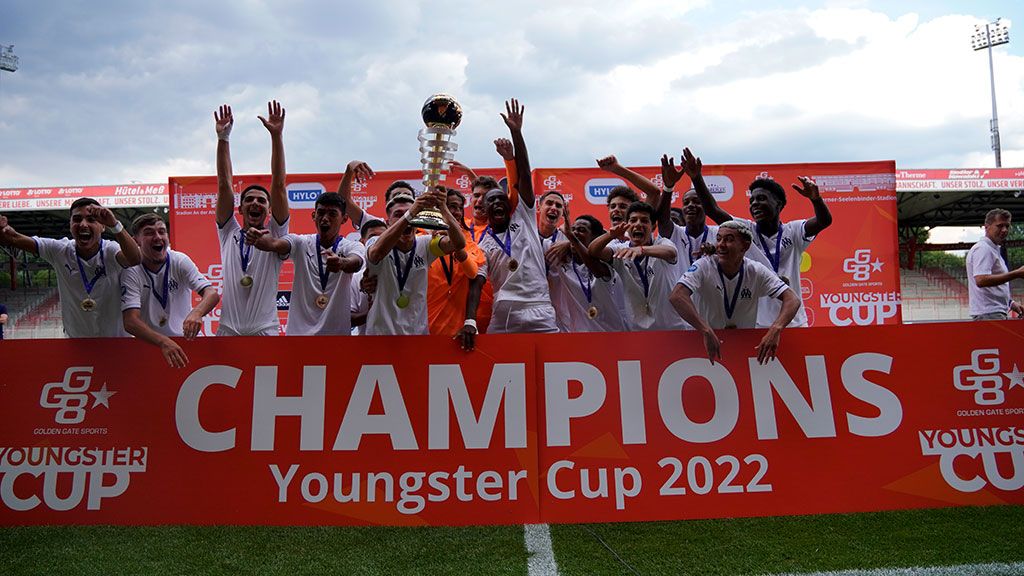 Eine Gruppe von jubelnden Fußballspielern hält einen Pokal vor einem Banner mit der Aufschrift "Champions Youngster Cup 2022".