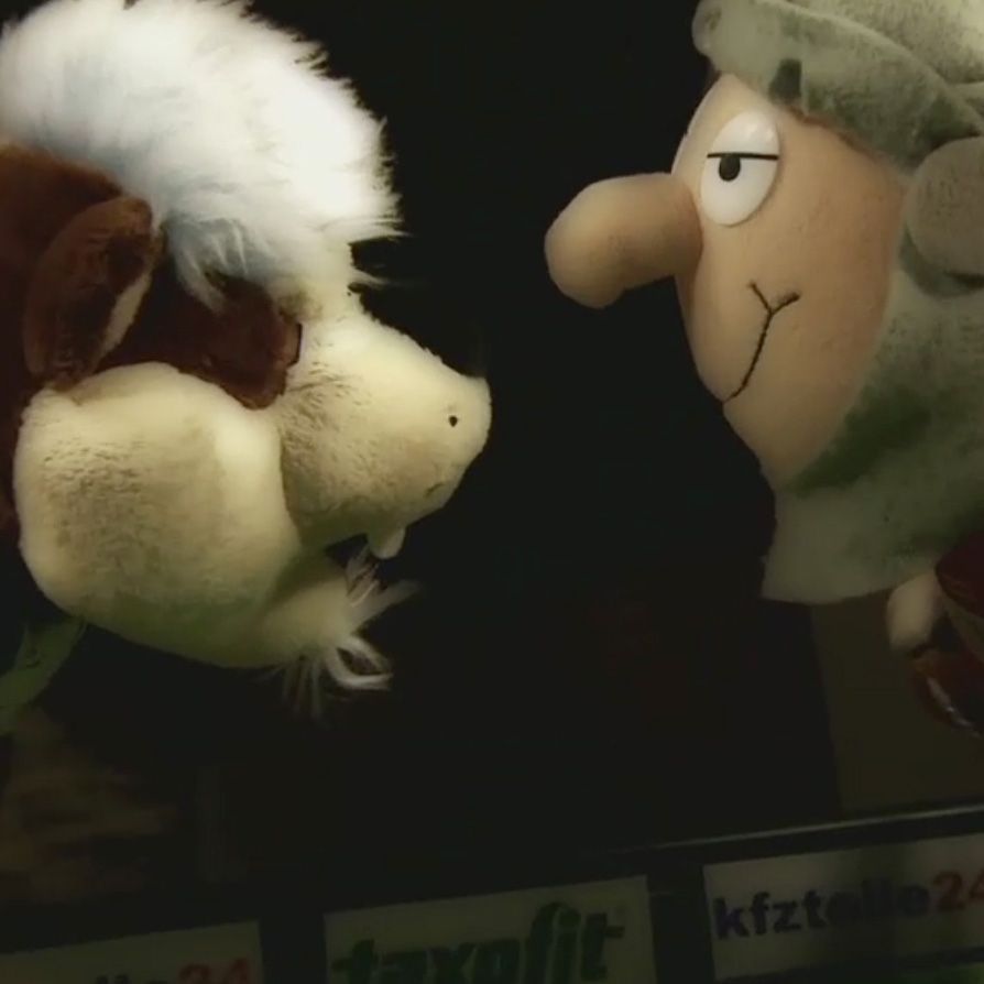 Zwei Handpuppen stehen sich gegenüber: eine tierische Figur und eine menschliche Figur mit einem neutralen Gesichtsausdruck.