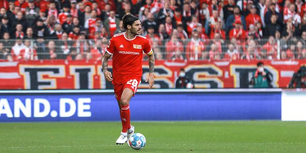 A soccer player in a red jersey with the number 29 dribbles the ball while fans cheer in the background.