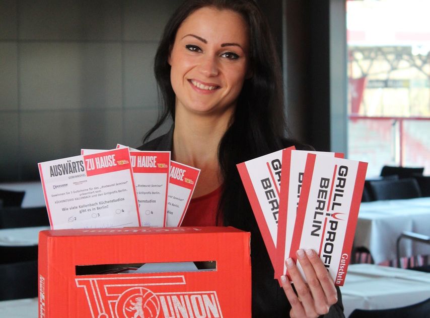Eine Frau hält ein Karton mit Werbung und Flyern in der Hand und steht vor einem Tisch in einem Restaurant.
