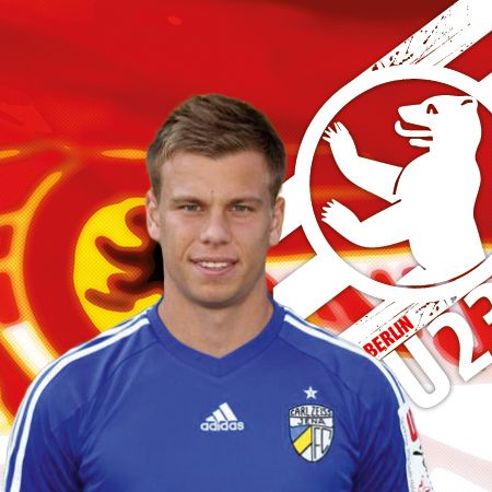 Ein sportlicher junger Mann in einem blauen Trikot, vor einem farbigen Hintergrund mit dem Logo eines Fußballvereins.