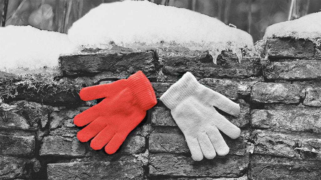 Rote und weiße Handschuhe hängen an einer steinernen Mauer, umgeben von Schnee und einer schwarz-weißen Umgebung.