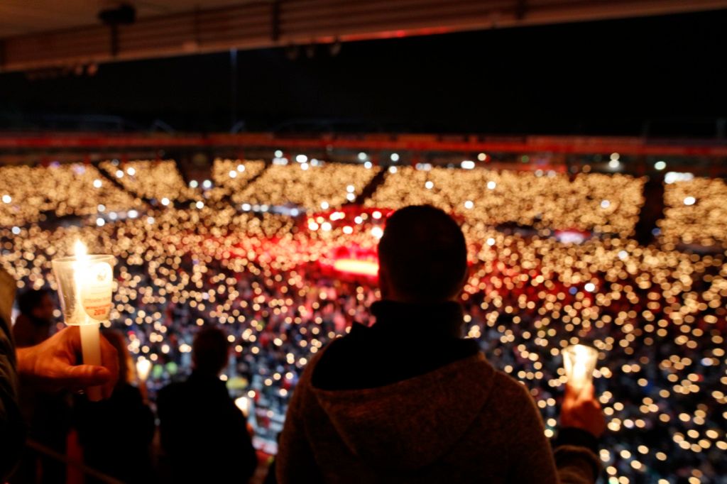 A person holds a candle in a stadium, surrounded by a crowd of shining candles in the dark.