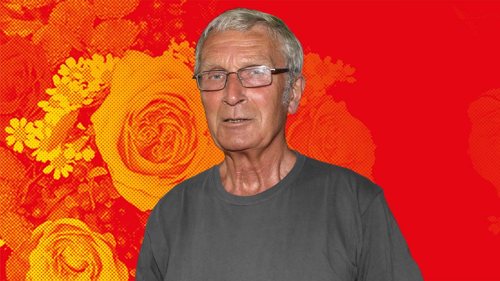 Ein älterer Mann mit Brille trägt ein graues T-Shirt vor einem floralen Hintergrund in Rot- und Gelbtönen.