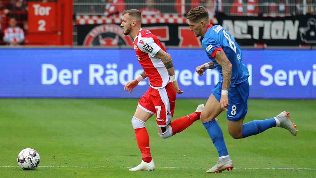 Two soccer players in action on the field, one in a red jersey and the other in a blue jersey.