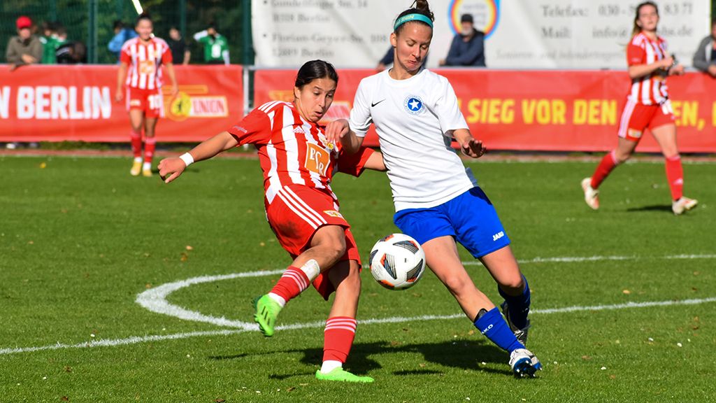 Two women are fighting for the ball on a green soccer field.