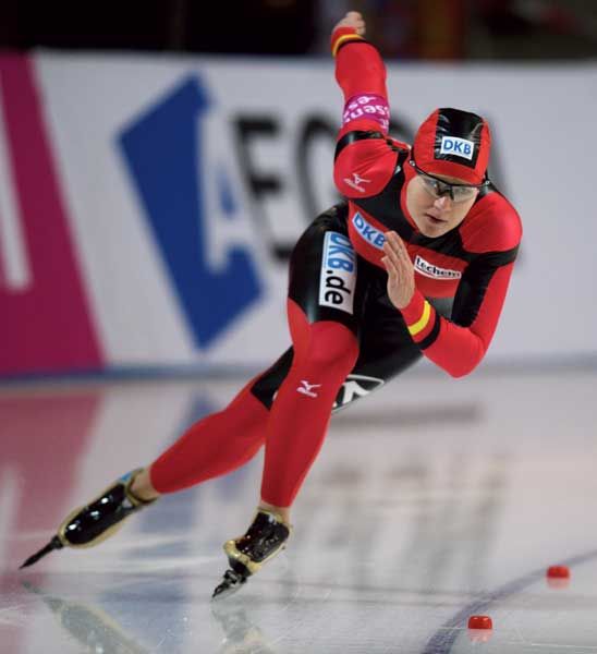Einschläfer beim Eisschnelllauf: Athlet in rot-schwarzer Kleidung, konzentriert auf der Eisbahn, mit einer Sportbrille und Skate-Schuhen.