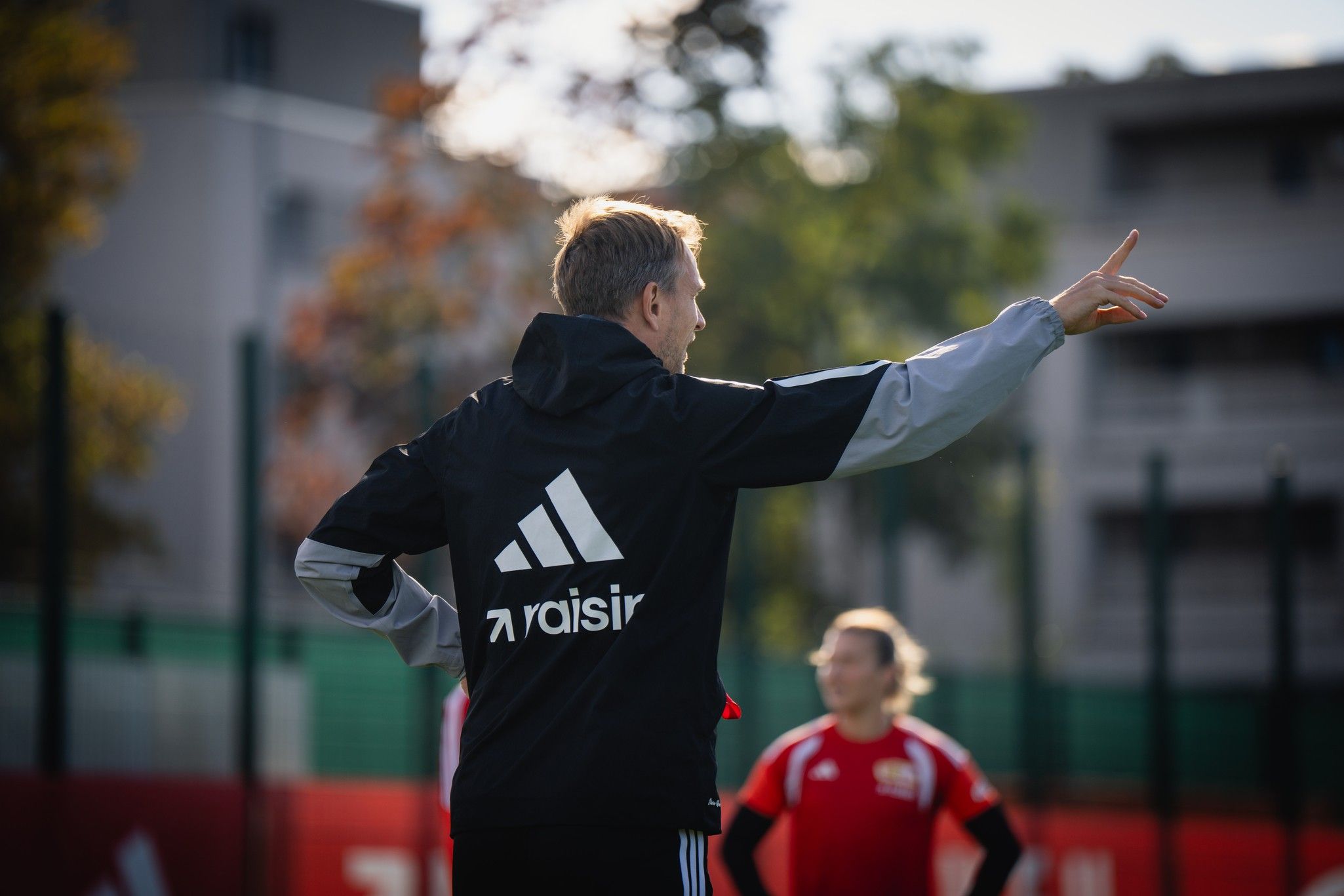 Trainer gibt Anweisungen während des Trainings auf dem Fußballplatz. Spieler im Hintergrund.