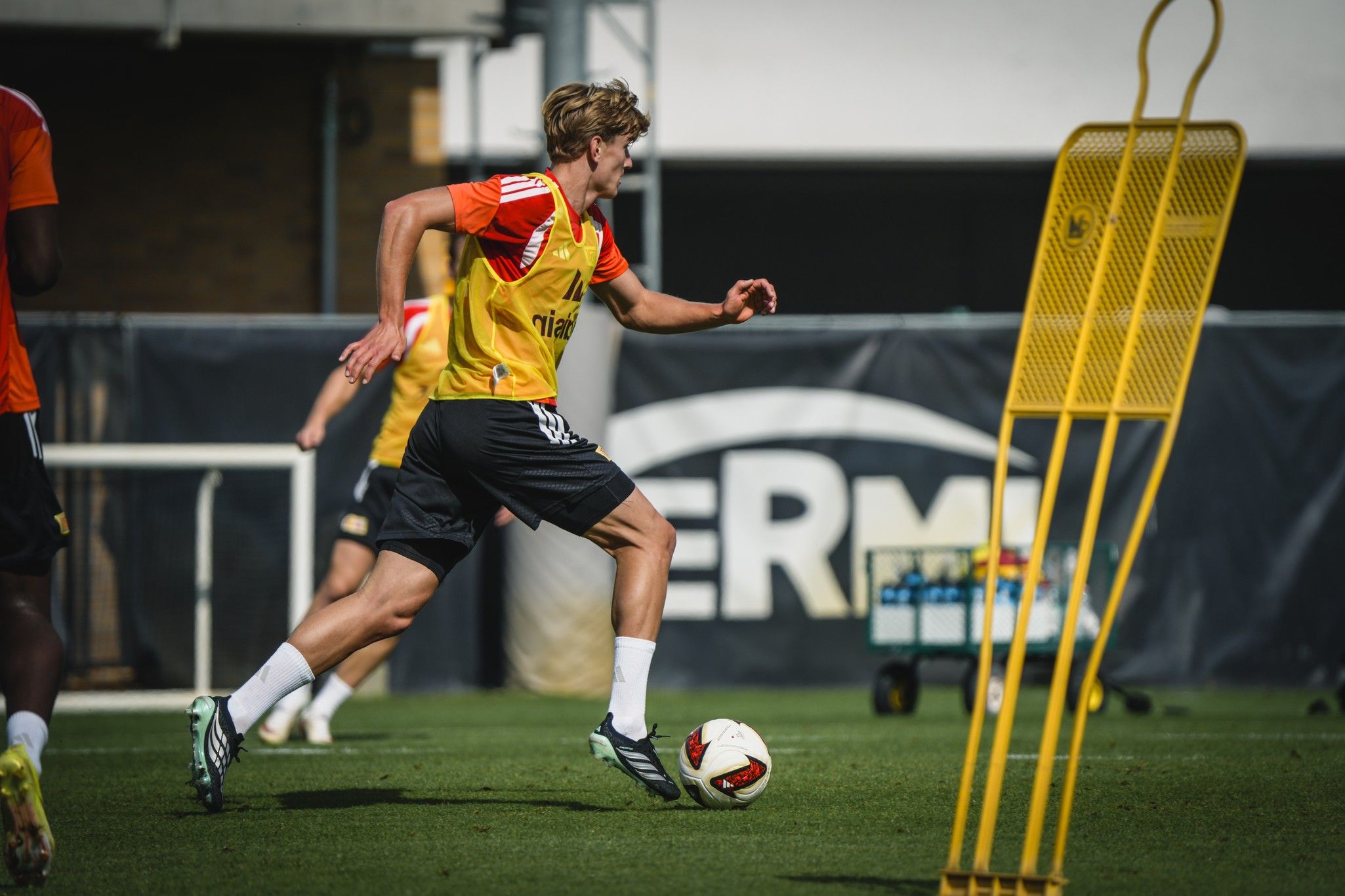 Spieler in gelber Trainingsausrüstung sprintet über das Feld, um einen Ball während des Trainings zu erreichen.