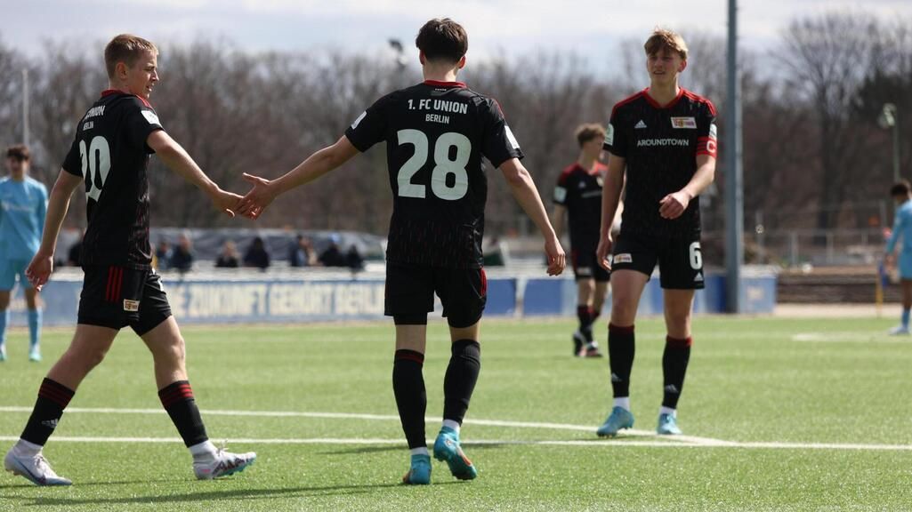 Zwei Fußballspieler des 1. FC Union Berlin geben sich die Hand, während ein dritter Spieler im Hintergrund steht.