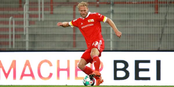 A soccer player in a red jersey is dribbling the ball on the field. In the background, there is an advertising board.