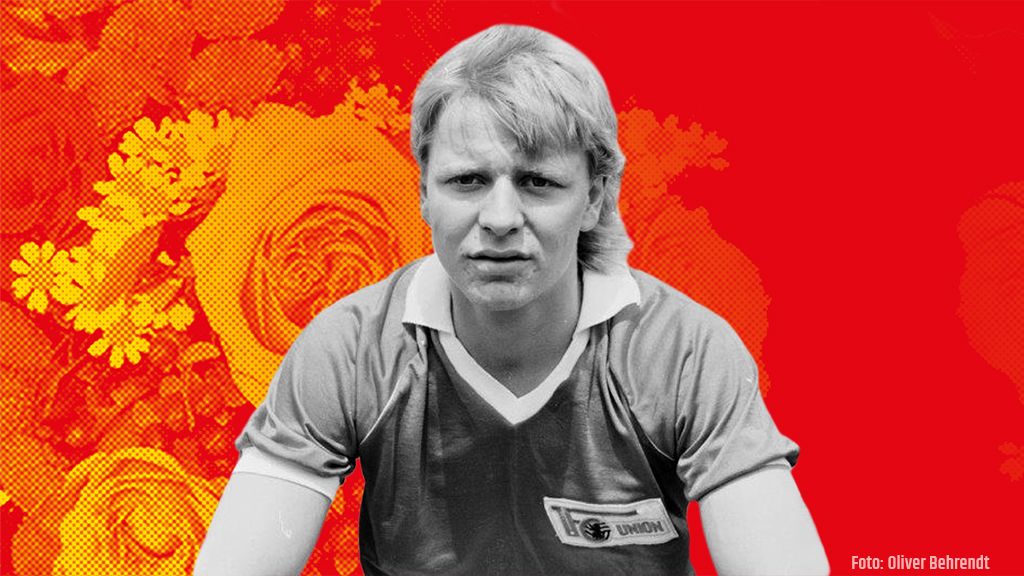 Schwarz-weiße Porträtaufnahme eines Mannes in einem Sporttrikot vor einem bunten Hintergrund mit Blumenmustern.