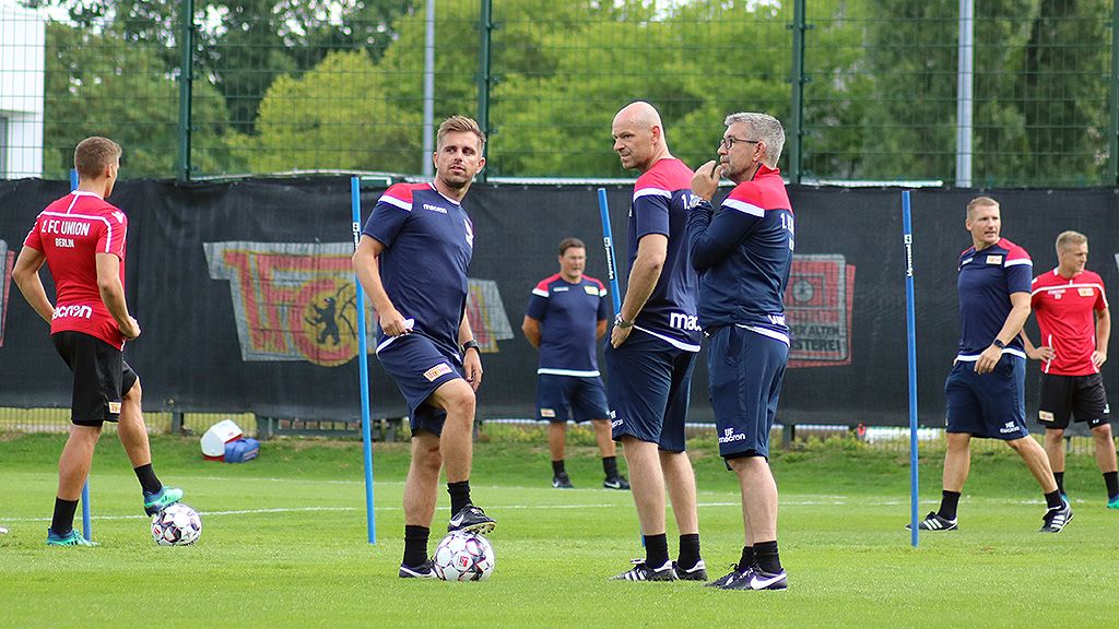Training session of a football team on a green field, with players in sportswear and coaching staff.