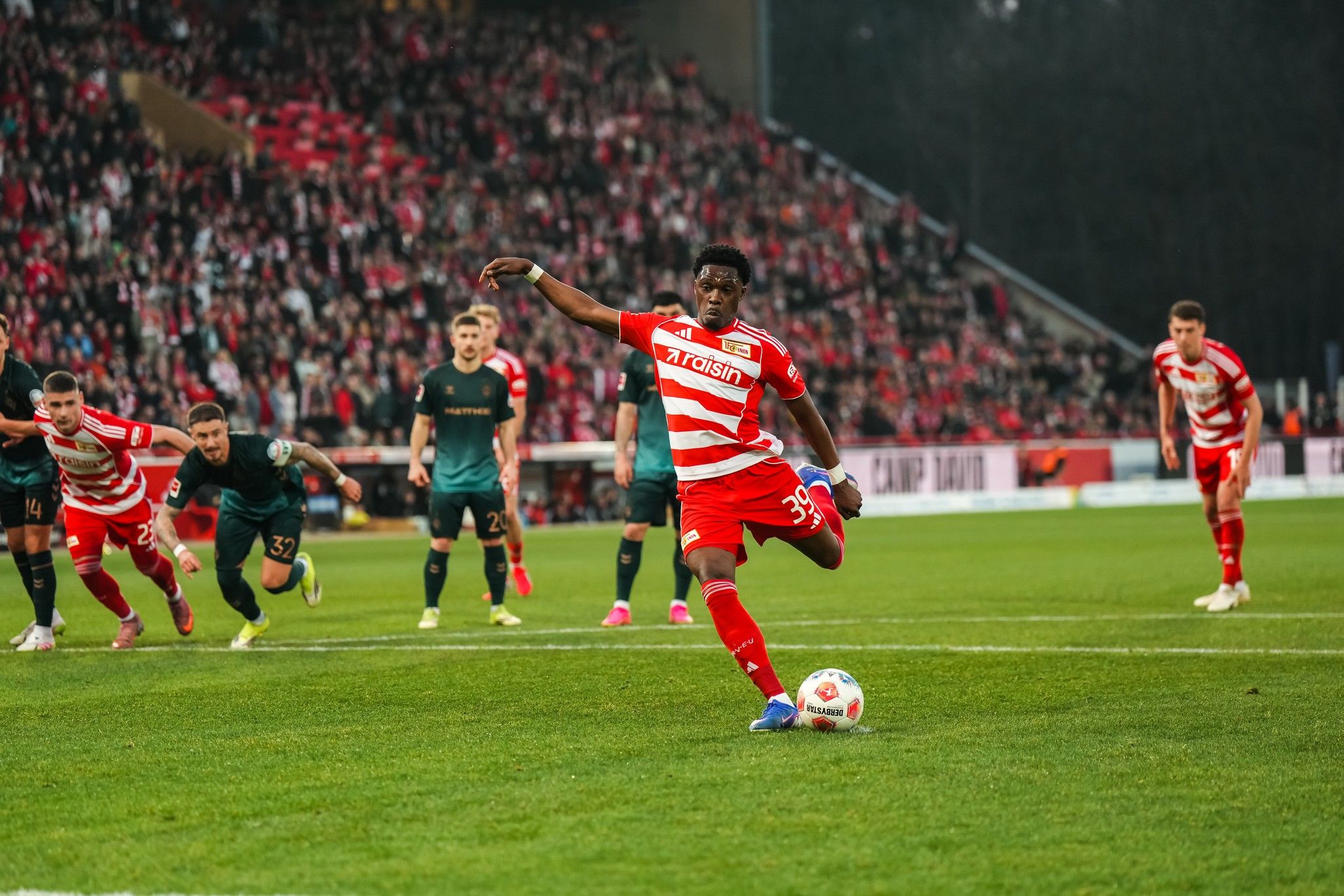 Spieler des FC Granada schießt einen Elfmeter, während Zuschauer im Hintergrund zuschauen.