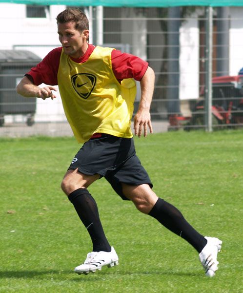 Ein Fußballspieler in einem gelben Trainingsoutfit läuft auf einem grünen Rasenfeld.