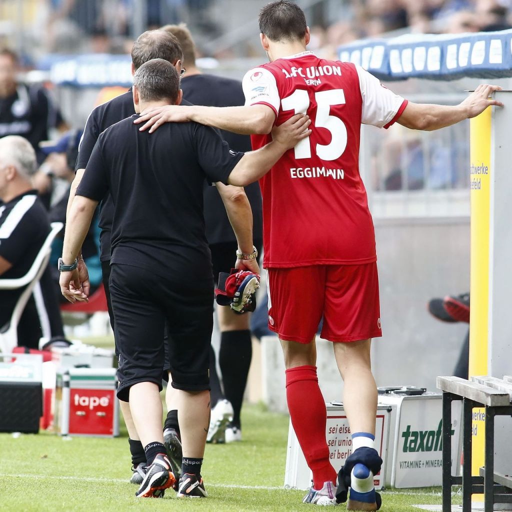 Ein Spieler mit der Nummer 15 in rotem Trikot verlässt das Spielfeld, umarmt von einem Trainer.