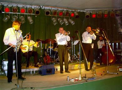 Eine Band spielt auf einer Bühne mit Trompeten und anderen Instrumenten, im Hintergrund sind Lichter und eine Schlagzeug-Set.