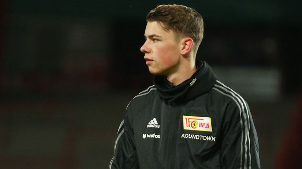 A young soccer player in a training jacket with the club logo looks thoughtful and focused.