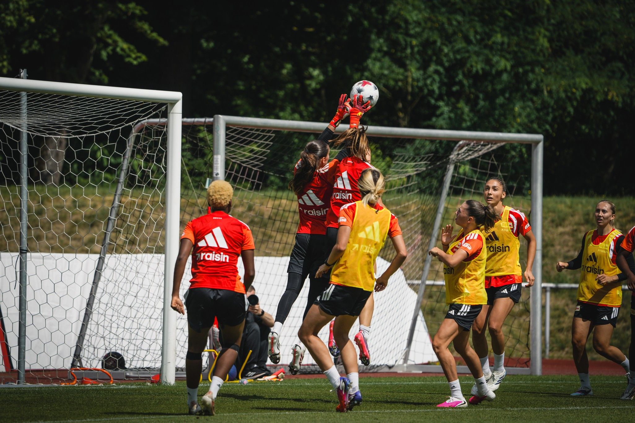 Eine Torhüterin springt hoch, um einen Ball während des Trainings zu fangen, während ihre Teamkolleginnen zuschauen.