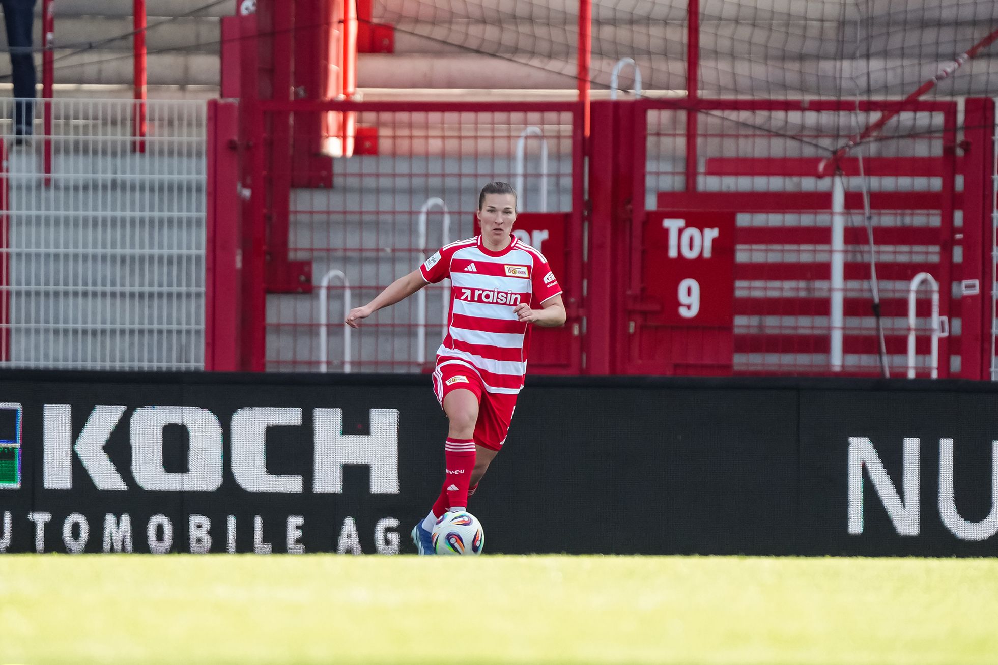 Eine Spielerin im roten Trikot mit weißen Streifen läuft auf dem Fußballplatz in Richtung des Tores.