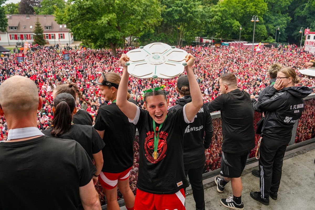 Ein jubelnder Spieler hält einen Pokal hoch, umgeben von einer großen Menschenmenge, die feiert.