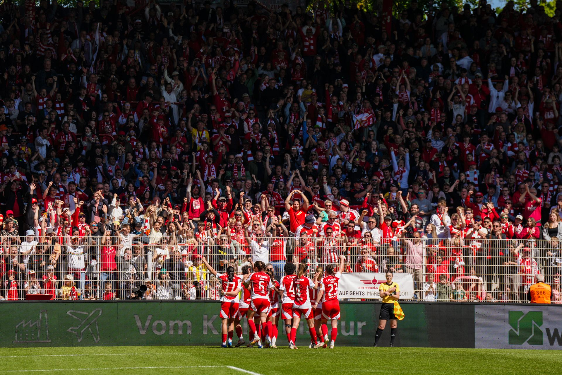 Fußballmannschaft jubelt vor einer jubelnden Menge in roten Trikots im Stadion.