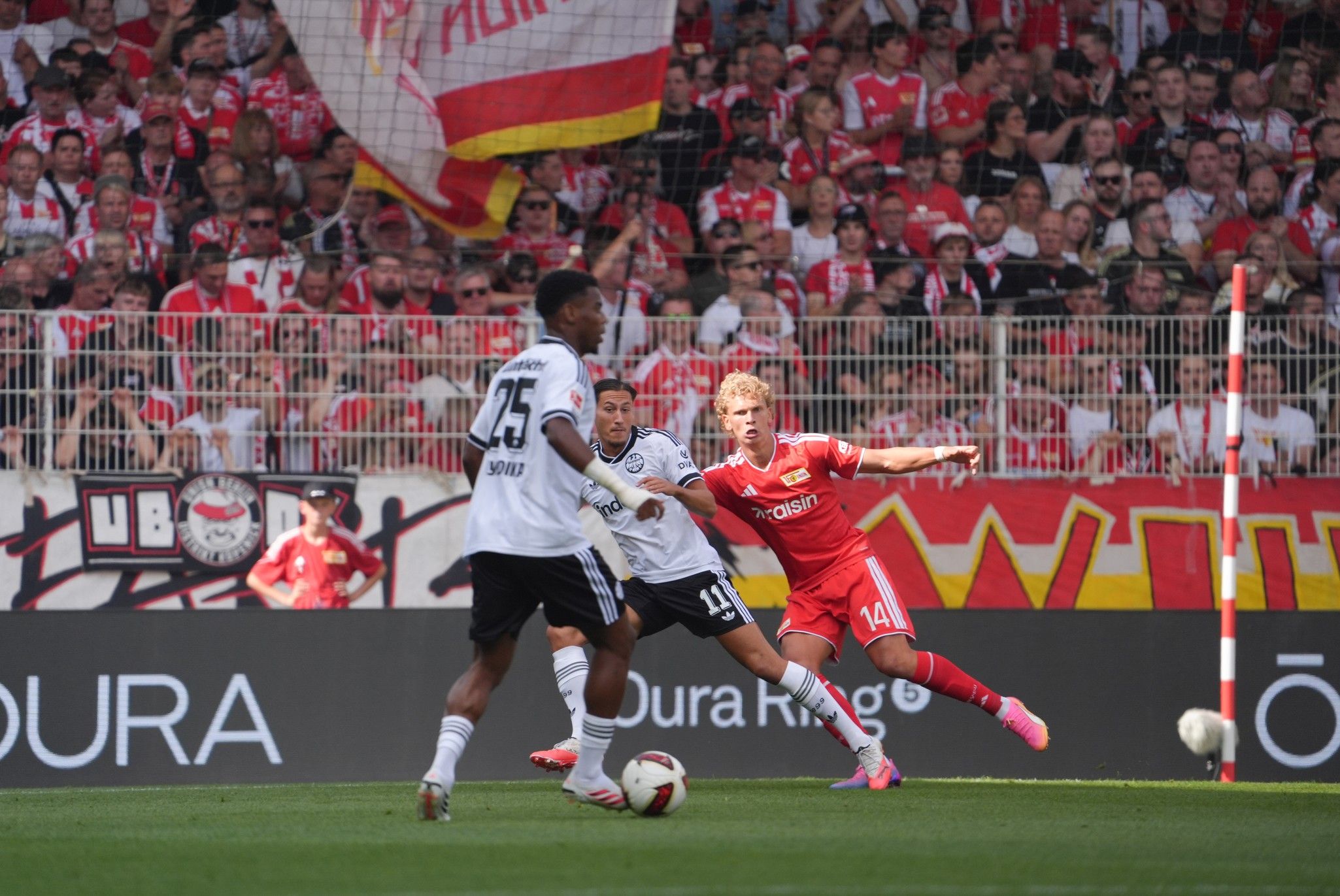 Ein Fußballspiel in einem Stadion mit Spielern im Wettkampf, Fans im Hintergrund, die Teamfahnen halten.