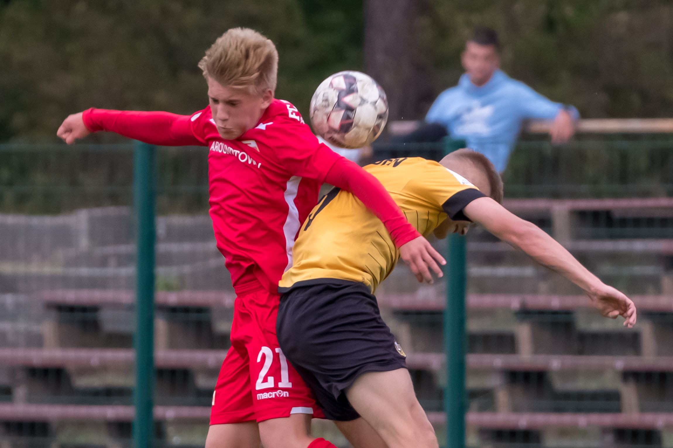 Zwei Fußballspieler in einem Zweikampf, einer in rotem Trikot, der andere in gelbem Trikot, während der Ball ins Spiel kommt.