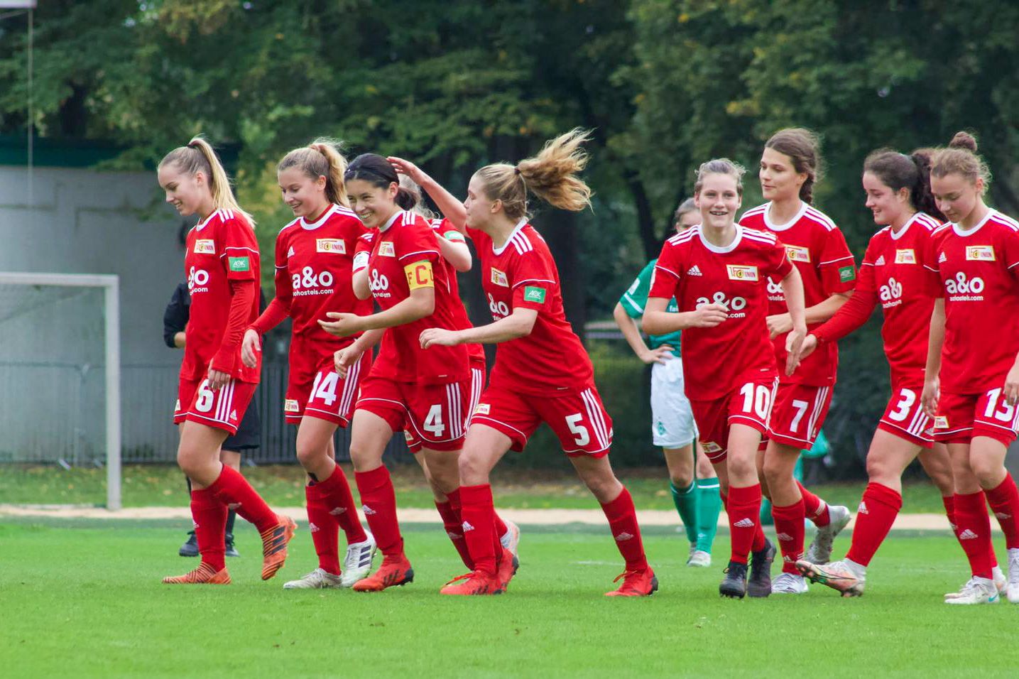 Eine Gruppe von Fußballspielerinnen in roten Trikots feiert einen Erfolg auf dem Spielfeld.