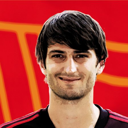 Porträt eines lächelnden Mannes mit mittellangen, dunklen Haaren vor einem rot-orangefarbenen Hintergrund.