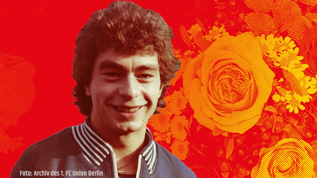 Ein junger Mann mit lockigem Haar lächelt vor einem roten Hintergrund mit Rosenmotiven.