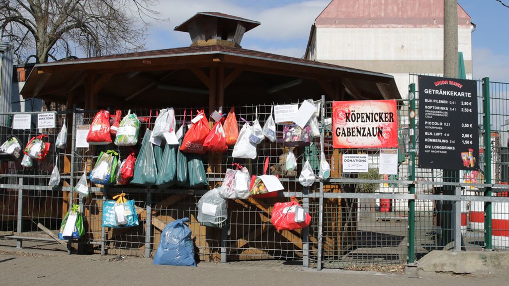 Gartenhaus mit einer Holzstruktur, umgeben von bunten Taschen und einem Preisboard für Getränke.