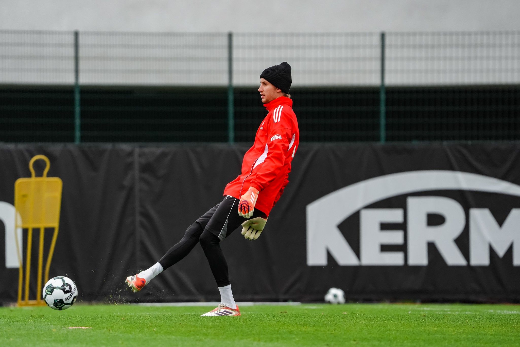 Ein Torwart in rot-training-outfit übt einen Abschlag auf einem Fußballplatz.