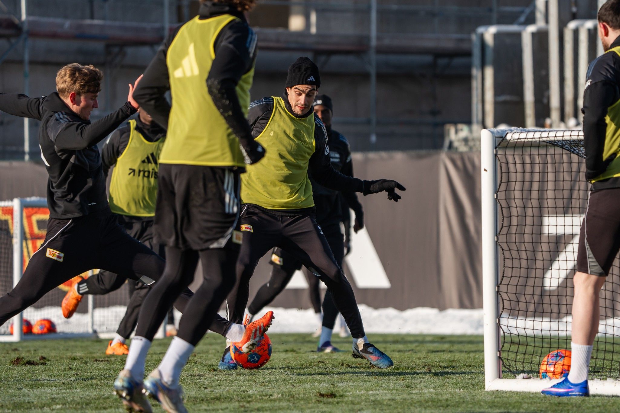 Fußballspieler in gelben Trainingswesten üben ein Schuss- und Passspiel auf einem Trainingsplatz.