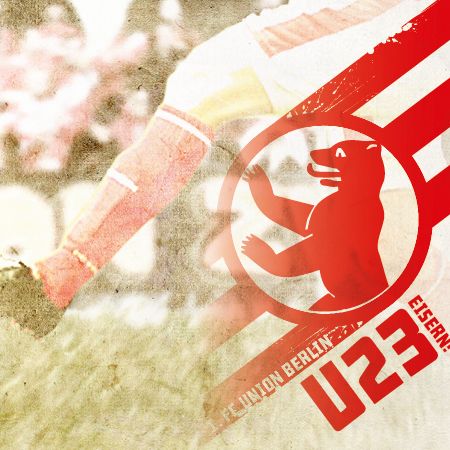 Ein verschwommenes Bild eines Fußballspielers in Aktion mit dem Union Berlin U23-Logo und rot-weißen Streifen im Hintergrund.