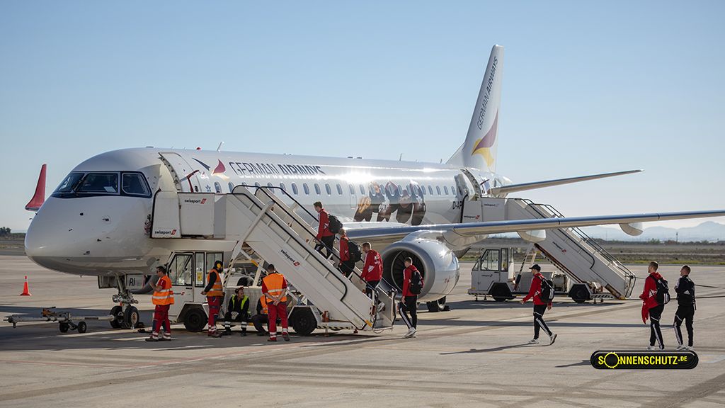 An airplane on the ground with passengers descending the steps while ground staff in safety vests assist.