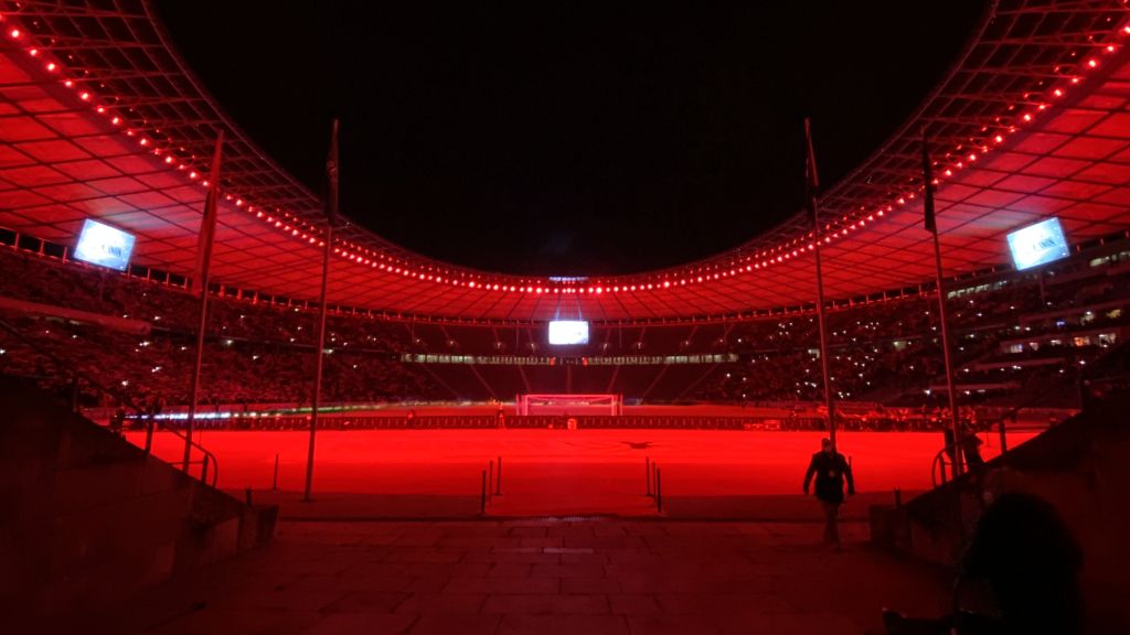 A stadium at night, illuminated in red light, with a view of the field and the spectator area.