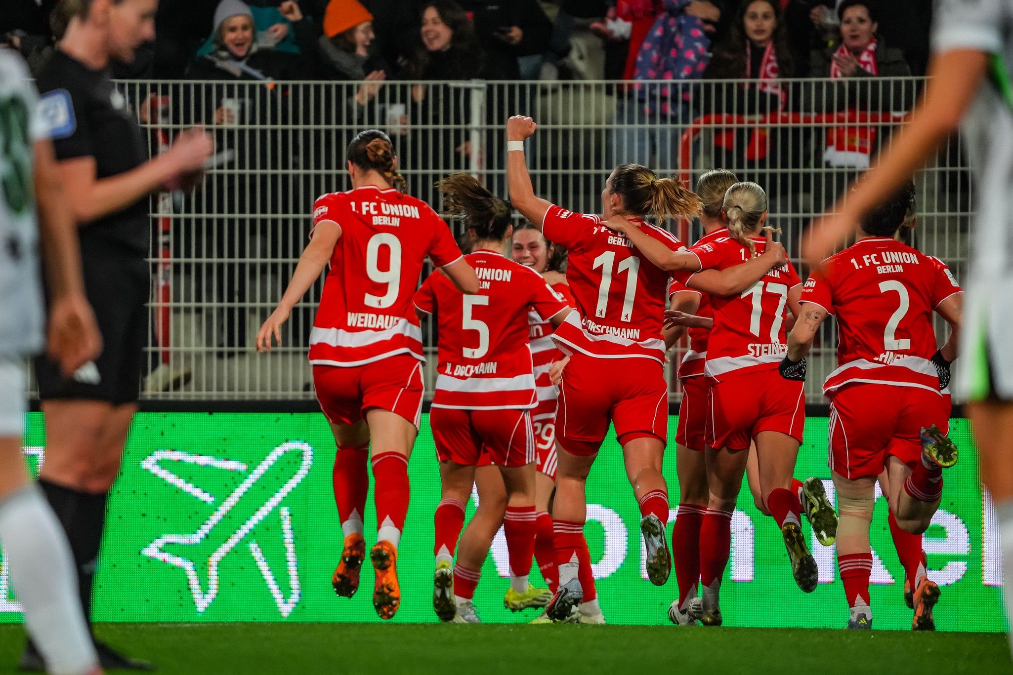 Eine Gruppe von Fußballspielerinnen in roten Trikots jubelt nach einem Tor in einem Stadion.