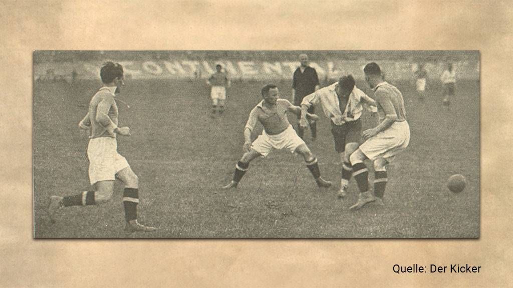 Schwarz-weiß Foto eines Fußballspiels mit drei Spielern in Aktion und einem Ball im zentralen Bereich.