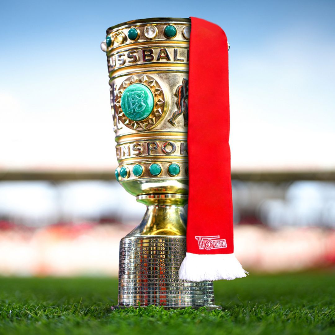 A football trophy with a red scarf, on green grass and a bright sky in the background.