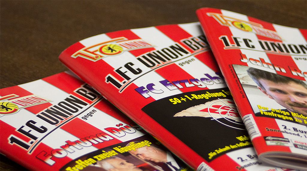 Drei Ausgaben einer Fanzeitschrift des 1. FC Union Berlin auf einem Tisch, rot-weiß gestreift mit verschiedenen Titeln.