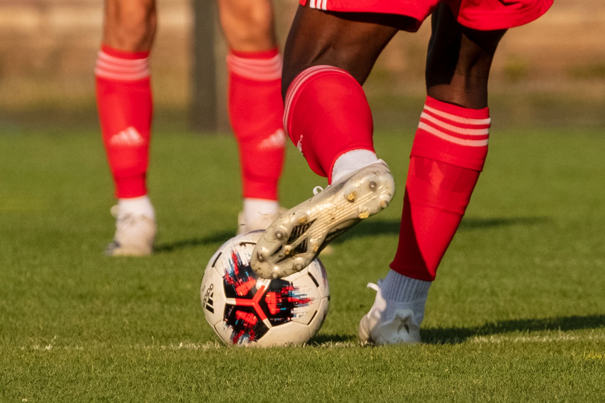 A football player in a red jersey kicks a colorful patterned ball on a grass field.