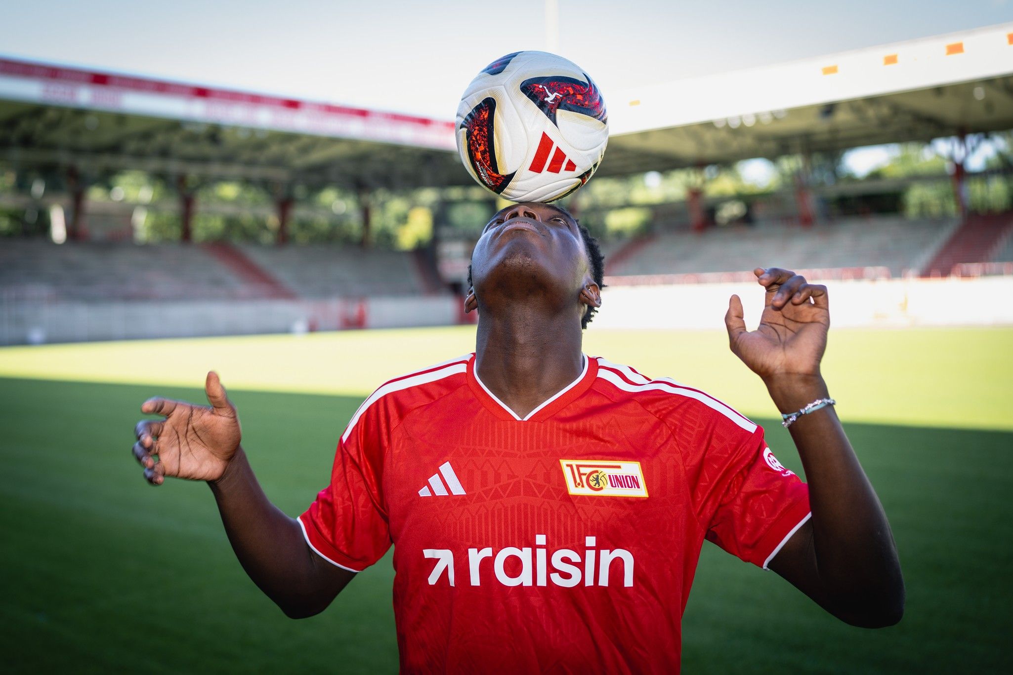 Ein Fußballspieler balanciert einen Fußball auf seinem Kopf, während er in einem Stadion steht.