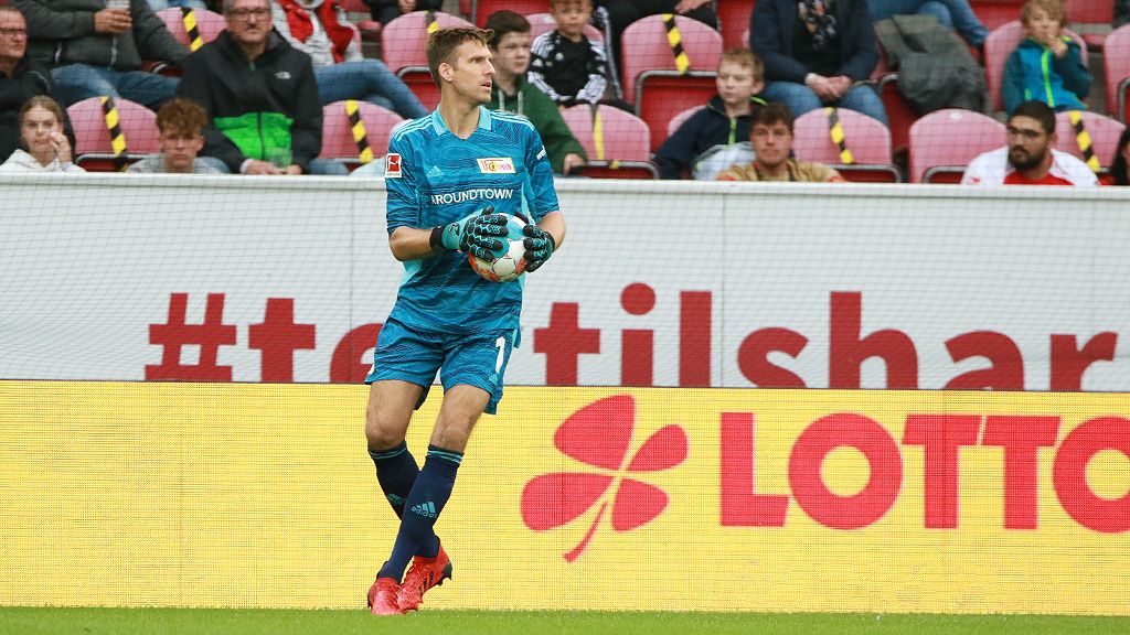 Goalkeeper in blue uniform saves the ball during a soccer game, spectators in the background.
