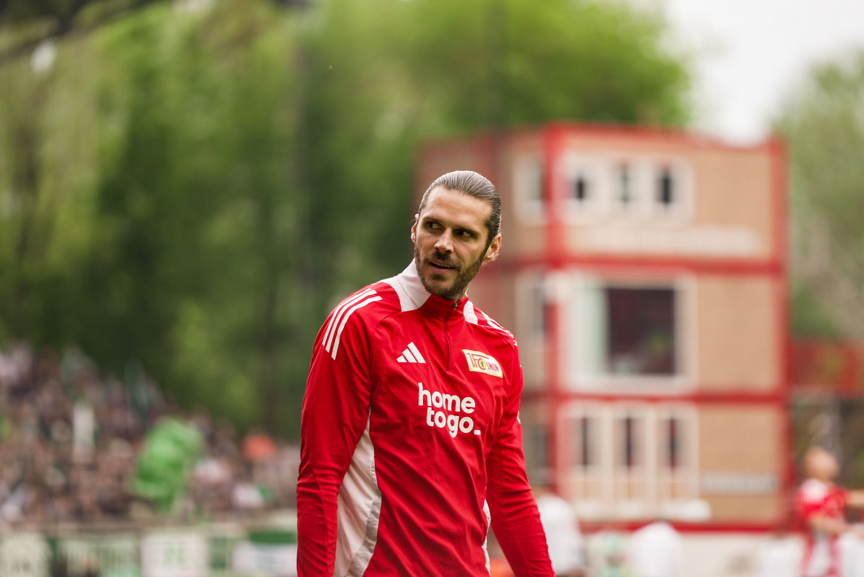 Un jugador de fútbol con una camiseta rojo-blanca con la inscripción "home.togo" está en el campo y mira a la cámara.
