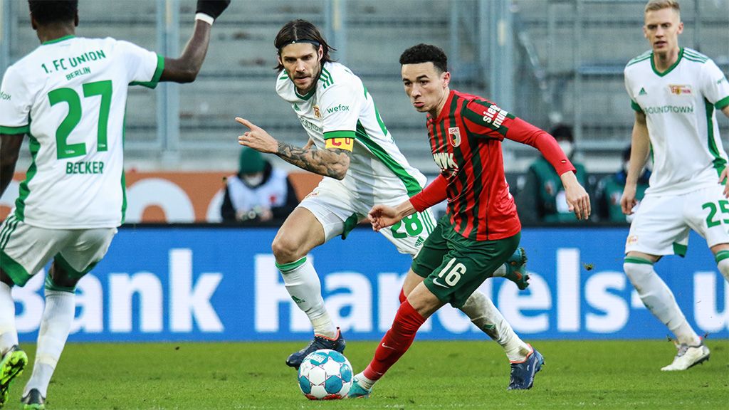 Zwei Fußballspieler im Wettkampf um den Ball, während zwei weitere Spieler im Hintergrund stehen.